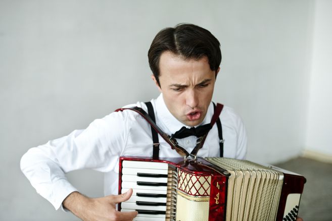 Ein Mann in weißem Hemd und Fliege spielt ein Akkordeon mit leidenschaftlichem Gesichtsausdruck.