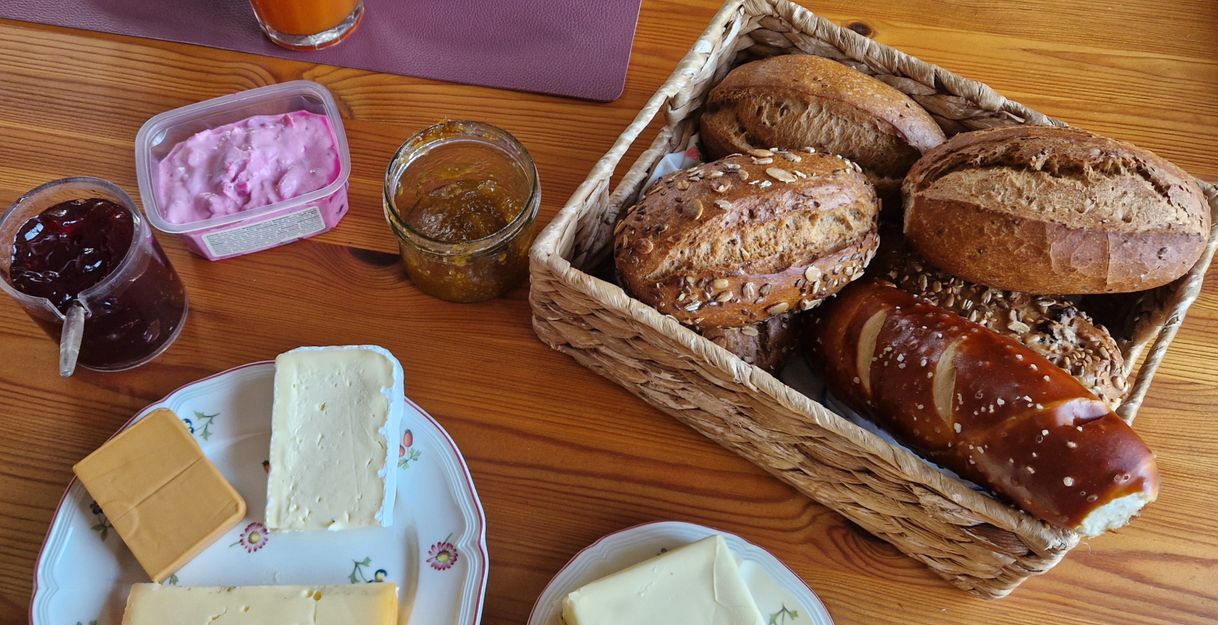 Frühstückstisch mit Brötchen, Käse, Marmelade und Getränken.