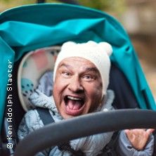 Ein lachender Mann in einem Kinderwagen mit weißer Mütze.