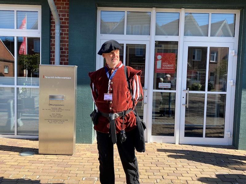 Ein Mann in historischer Kleidung steht vor einem Gebäude mit der Aufschrift 'Tourist-Information'.