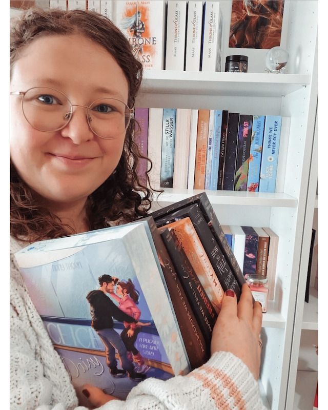 Person hält Bücher vor einem Bücherregal.