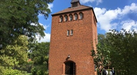 Backsteinturm mit Bäumen und blauem Himmel im Hintergrund.