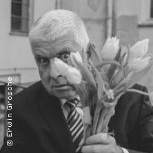 Ein Mann mit grauen Haaren hält einen Strauß Tulpen und schaut überrascht in die Kamera.