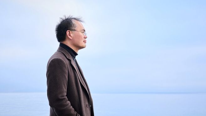 Ein Mann im Profil, der auf das Meer blickt, vor einem blauen Himmel.