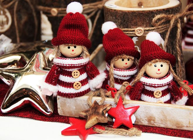 Drei weihnachtliche Puppen in rot-weißen Strickoutfits mit Mützen, umgeben von Sternen und Dekorationen.