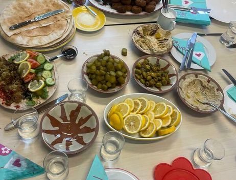 Tisch mit Speisen beim Interkulturellen Frauenfrühstück: Fladenbrot, Dips, Oliven, Gurken, Tomaten, Zitronenscheiben und Wassergläser, dazu Hände von Teilnehmenden.