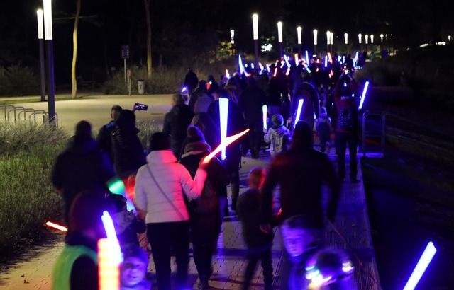 Menschenmenge bei Nacht mit leuchtenden LED-Stäben in verschiedenen Farben.