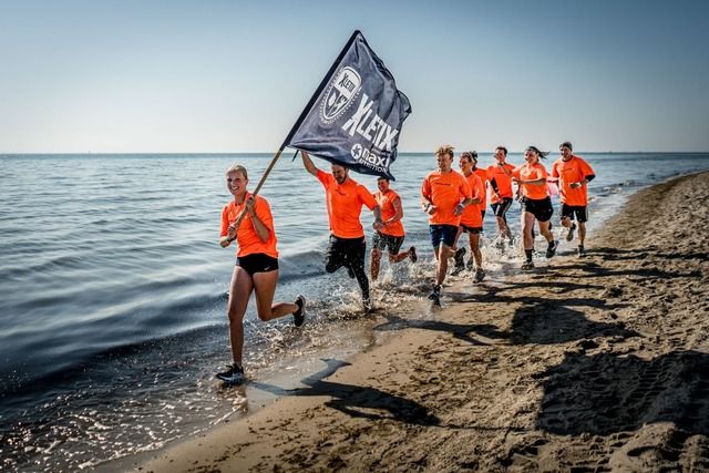 Eine Gruppe von Menschen in orangefarbenen T-Shirts läuft am Strand entlang, wobei eine Person eine XLETIX-Flagge trägt.