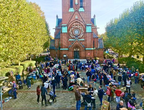 Ein belebter Flohmarkt auf einem Kirchplatz mit vielen Ständen und Besuchern vor einer großen Backsteinkirche.