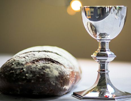 Ein silberner Kelch neben einem Laib Brot auf einem Tisch.