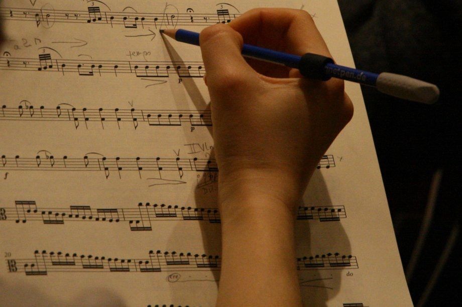 Aufnahme von einer Hand, die gerade mit einem Stift was auf einem Notenblatt notiert
