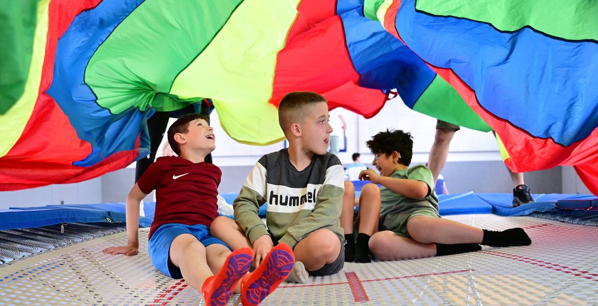 Drei Kinder sitzen unter einer bunten Plane.