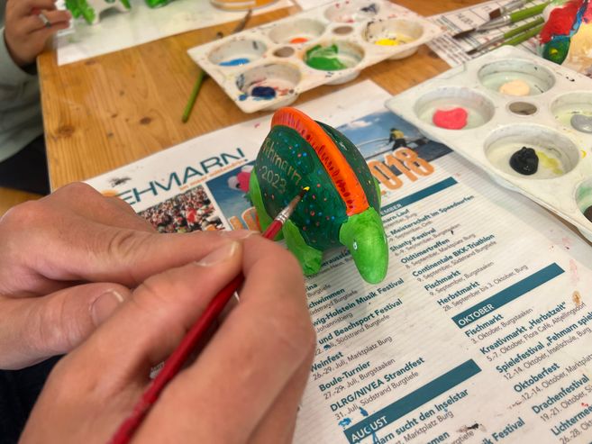 Person bemalt eine grüne Porzellanfigur mit einem Pinsel.