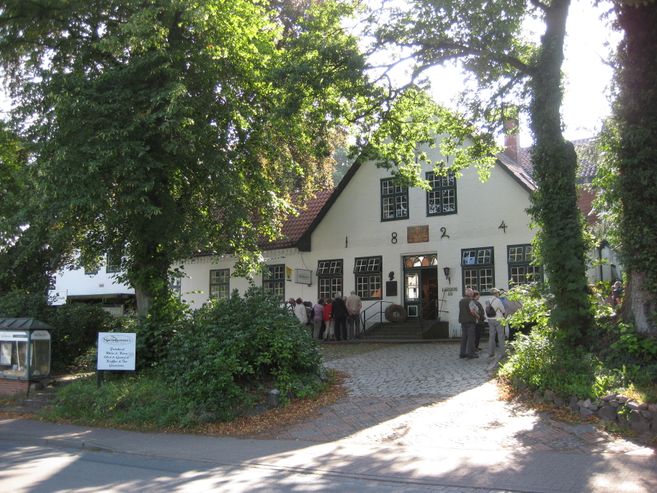 Ein historisches Gebäude in Worpswede, umgeben von Bäumen, mit Menschen, die davor stehen.