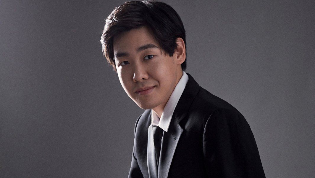 Porträt eines jungen Mannes in einem Anzug vor grauem Hintergrund.