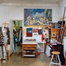 Ein Künstleratelier mit Gemälden an der Wand und Malutensilien im Raum verteilt.