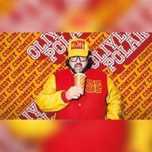 Person in roter und gelber Jacke mit einem Getränk vor einer Wand mit dem Schriftzug 'Oliver Polak Comedy'.