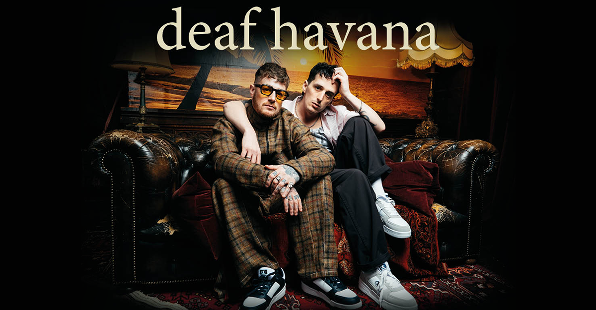 Zwei Männer sitzen auf einem Ledersofa vor einem Strandbild mit der Aufschrift 'deaf havana'.