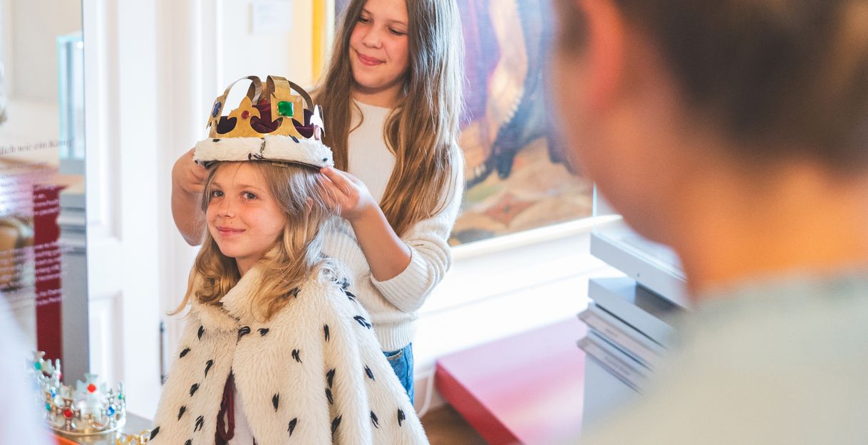 Zwei Mädchen spielen im Museum mit Krone und Umhang.