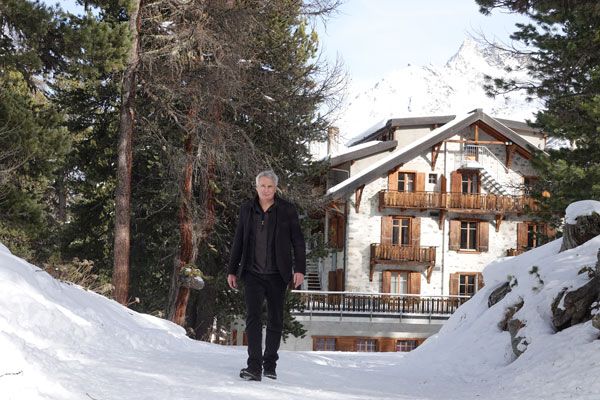 Mann im Schnee vor einem Chalet in den Bergen.