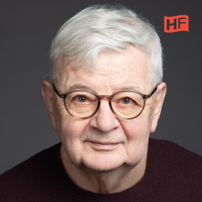 Porträt eines älteren Mannes mit Brille und grauen Haaren vor grauem Hintergrund.