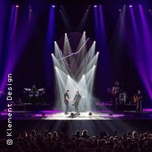 Bühnenauftritt einer Band mit beeindruckender Lichtshow und Publikum im Vordergrund.