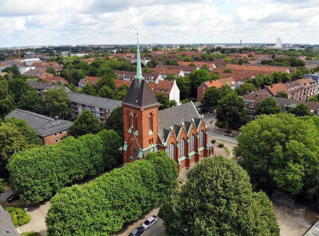 Luftaufnahme einer roten Backsteinkirche mit grünem Dach inmitten einer Wohngegend mit vielen Bäumen.