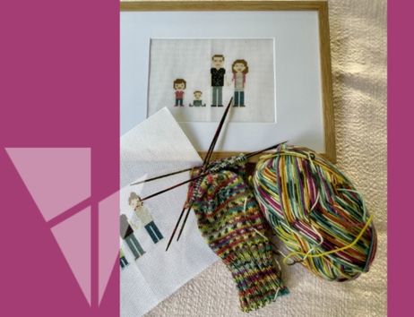 Ein Stickbild einer Familie in einem Rahmen, daneben ein unfertiges Strickprojekt mit buntem Garn und Stricknadeln.