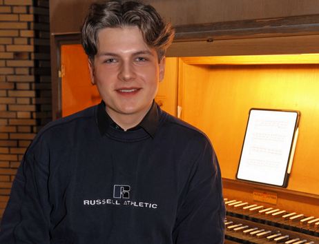 Ein junger Mann sitzt vor einer Orgel mit Notenblatt im Hintergrund.
