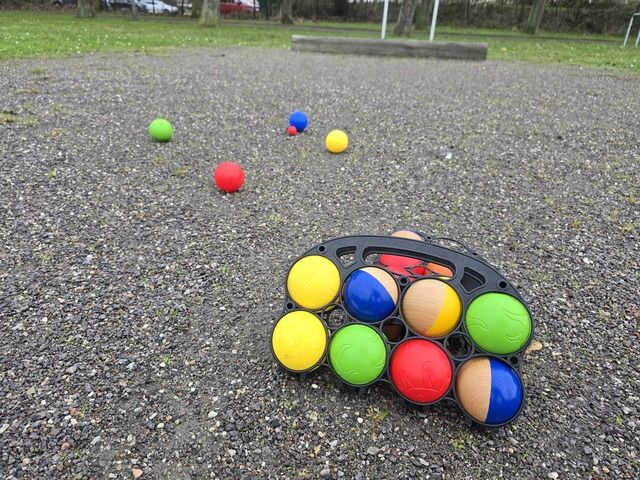 Boccia-Kugeln auf einem Kiesplatz mit einem Tragegestell im Vordergrund.