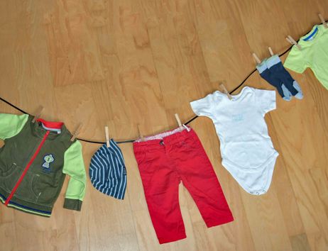 Kinderkleidung hängt an einer Wäscheleine auf einem Holzboden.