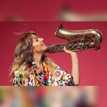 Eine Frau hält ein Saxophon vor einem roten Hintergrund.