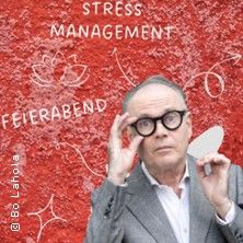 Ein Mann mit Brille vor einer roten Wand mit den Worten 'Stress Management' und 'Feierabend'.