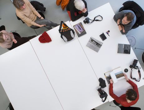 Menschen sitzen um einen großen Tisch mit Kameras und Fotobüchern.
