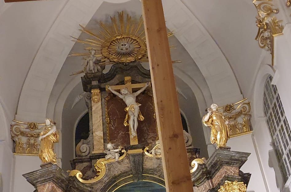 Innenansicht der St. Michaelis Kirche mit einem großen Holzkreuz im Vordergrund und einem kunstvollen Altar im Hintergrund.