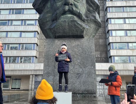 A Kid stands on a base in front of a huge statue of Karl Marx.