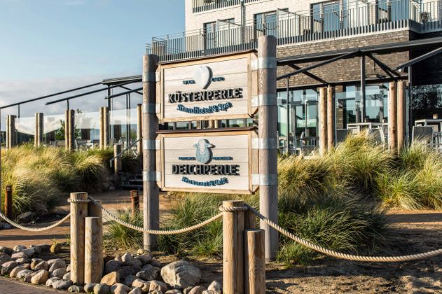 Eingangsschild des Küstenperle Strandhotel & Spa und Deichperle Restaurant & Café.