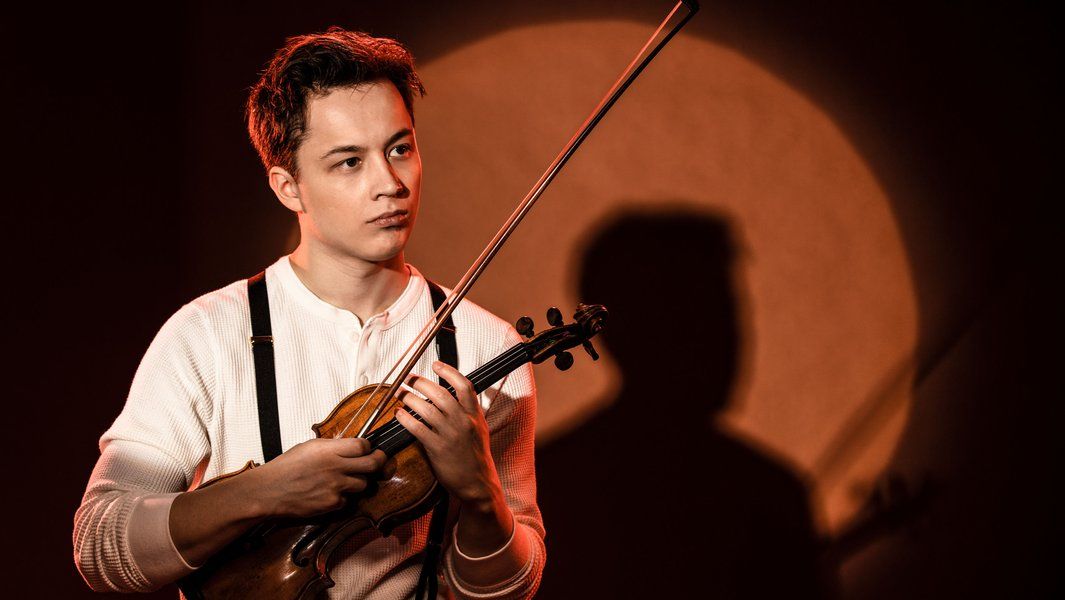 Ein Mann mit Geige vor einem runden Lichtschein.