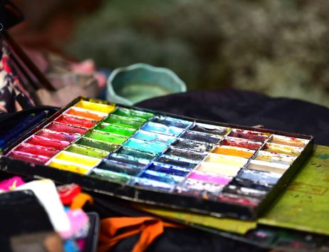Eine bunte Palette mit verschiedenen Farben und Pinseln auf einem Tisch in einer kreativen Werkstatt.