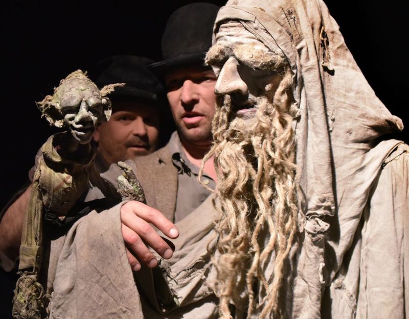 Zwei Männer in Kostümen, einer hält eine Puppe, die wie eine Fantasy-Kreatur aussieht.