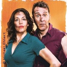 Ein Mann und eine Frau stehen nebeneinander vor einem orangefarbenen Hintergrund. Beide schauen überrascht in die Kamera.