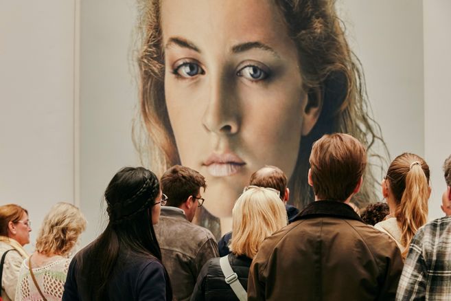 Besucher betrachten ein großes Porträt einer Frau in einer Ausstellung.