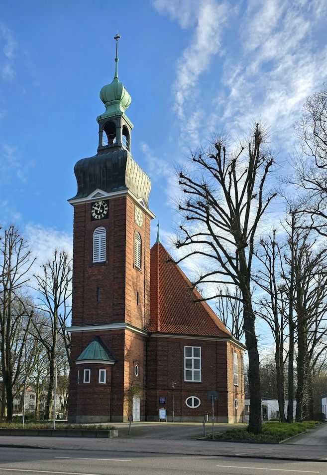 Backsteinkirche mit Turm und grünem Dach vor blauem Himmel.
