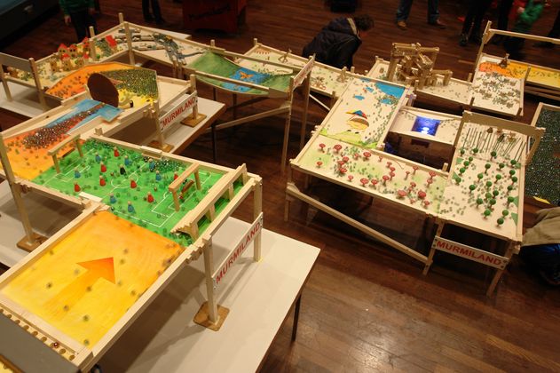 große Murmelbahn mit vielen unterschiedlich gestalteten Feldern, über die Mengen an Glasmurmeln kullern