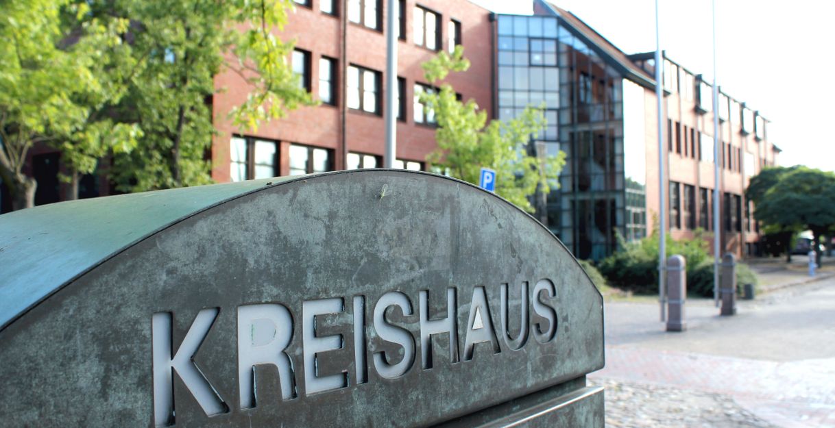 Ein Schild mit der Aufschrift 'Kreishaus' vor einem modernen Backsteingebäude mit Glasfassade.