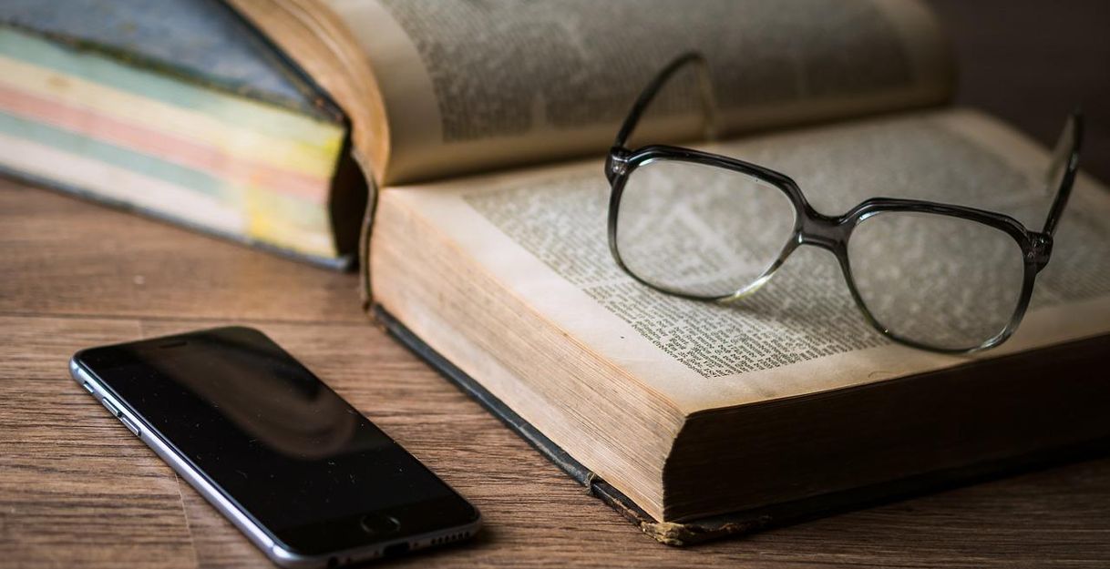 Smartphone, Brille und Buch auf einem Holztisch