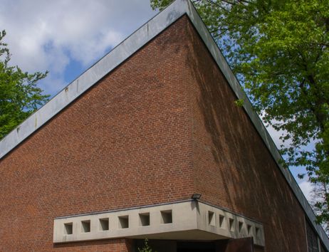 Backsteinfassade eines modernen Gebäudes mit geometrischen Formen und Bäumen im Hintergrund.