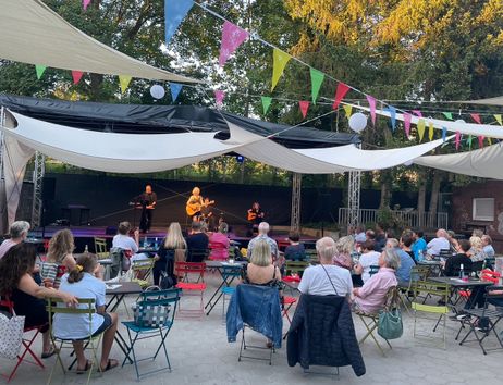 Open-Air-Konzert mit Zuschauern auf bunten Stühlen unter Wimpelgirlanden.