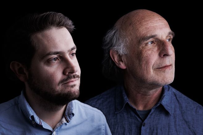 Zwei Männer im Porträt vor schwarzem Hintergrund, links ein jüngerer Mann mit Bart, rechts ein älterer Mann mit Glatze, beide im Profil nach rechts blickend.