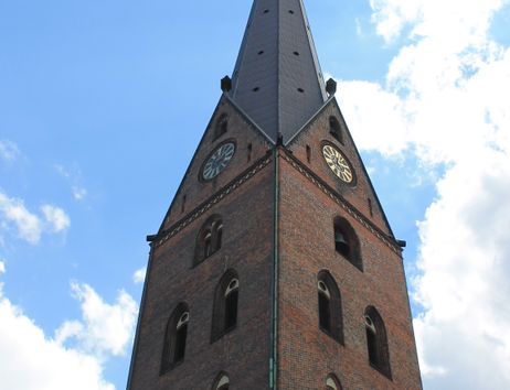 Spitz zulaufender Kirchturm der St. Petri Kirche vor blauem Himmel mit Wolken.